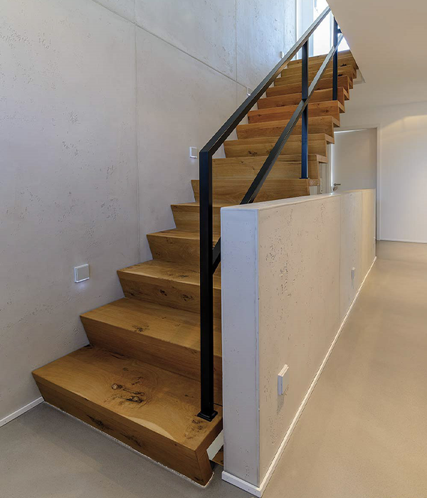 Geradläufige Holztreppe mit schwarzem Stahlgeländer neben heller Betonwand in modernem Hausflur