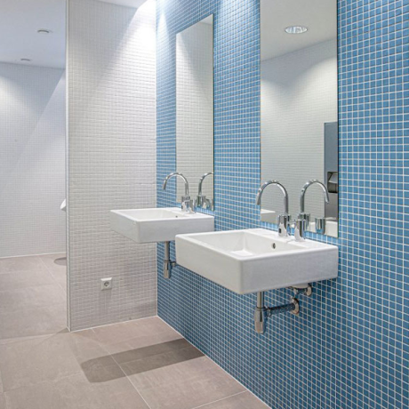 Heller Waschraum mit zwei weißen Wandwaschbecken vor blauer Mosaikwand und großen Spiegeln